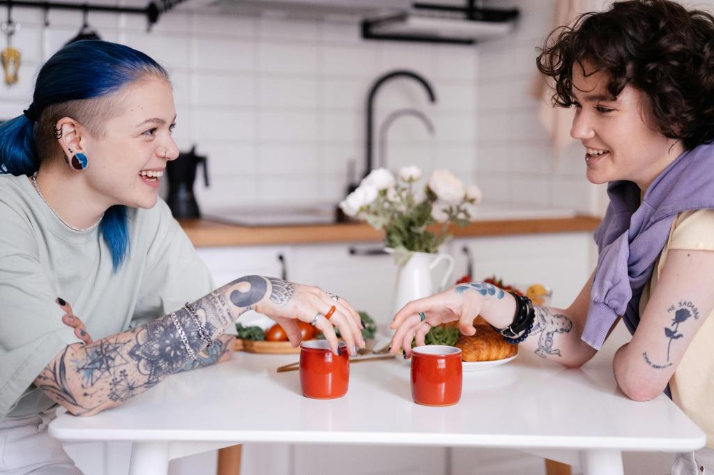 two queer people talking, smiling, over a cup of coffee